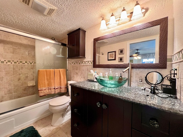 full bathroom featuring vanity, combined bath / shower with glass door, ceiling fan, toilet, and tile walls