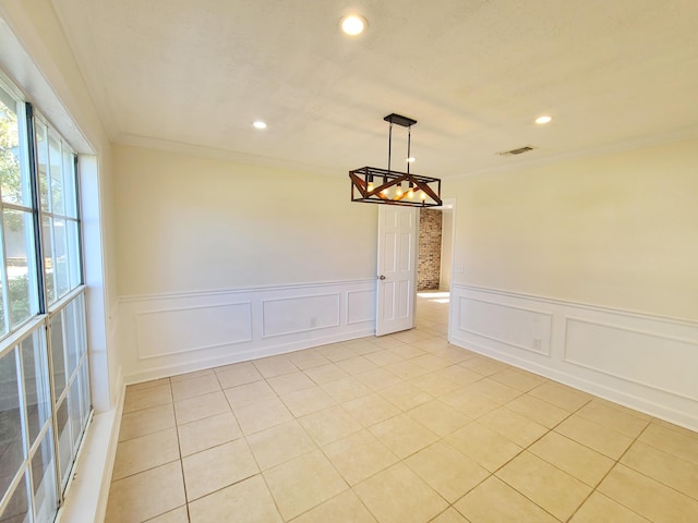 empty room featuring crown molding, light tile patterned floors, and an inviting chandelier