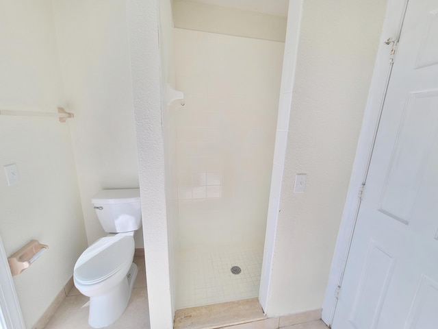 bathroom with a tile shower, toilet, and tile patterned floors