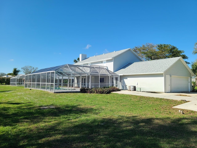 rear view of house with a lawn, glass enclosure, a garage, and a pool