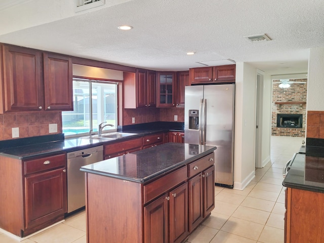 kitchen featuring a center island, sink, a textured ceiling, a fireplace, and stainless steel appliances