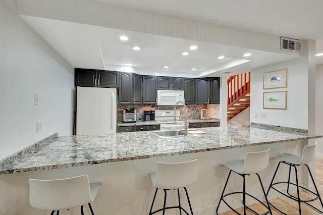 kitchen with kitchen peninsula, a kitchen bar, white appliances, and sink