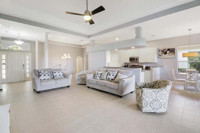 living room featuring a tray ceiling, a towering ceiling, light tile patterned floors, and ceiling fan with notable chandelier