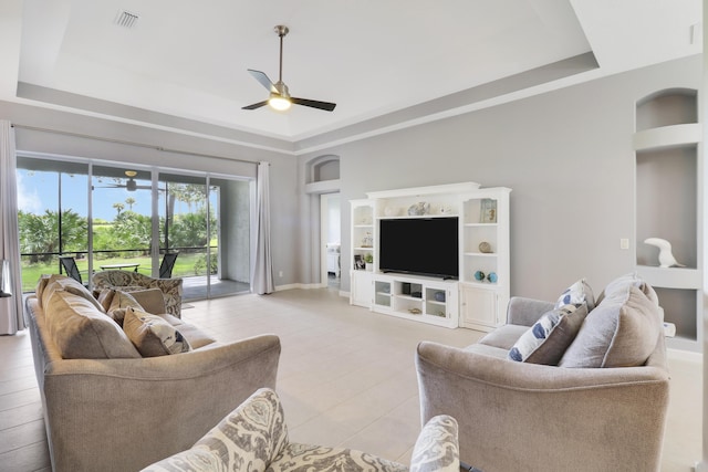 living room featuring ceiling fan, a raised ceiling, and built in features