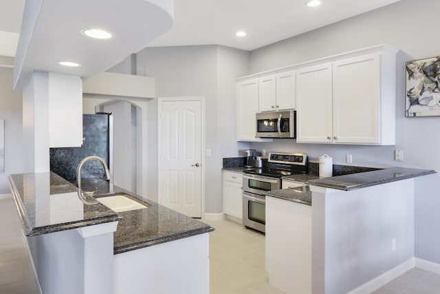 kitchen featuring kitchen peninsula, stainless steel appliances, sink, dark stone countertops, and white cabinetry