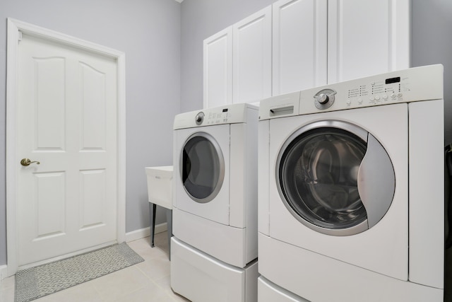 laundry room featuring washing machine and dryer, light tile patterned floors, and cabinets