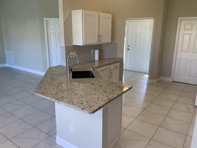 kitchen with light stone counters, white dishwasher, a peninsula, a sink, and marble finish floor