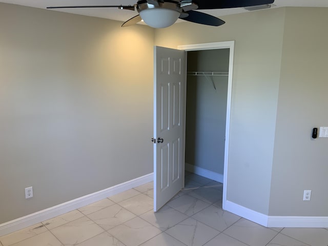 unfurnished bedroom with a closet, marble finish floor, baseboards, and a ceiling fan