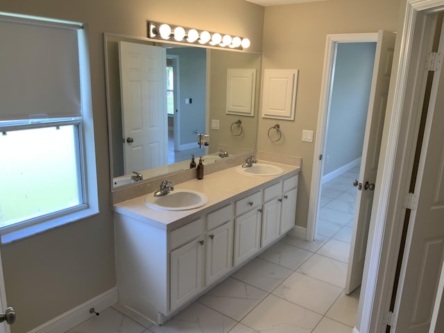 full bathroom featuring marble finish floor, double vanity, a sink, and baseboards