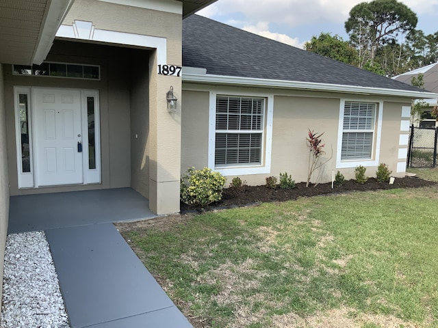 entrance to property featuring stucco siding, roof with shingles, and a yard