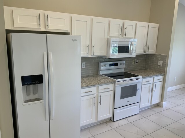 kitchen featuring light stone counters, white appliances, white cabinets, and backsplash