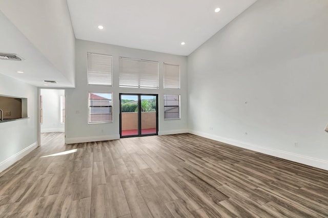 unfurnished living room with light hardwood / wood-style flooring and a towering ceiling