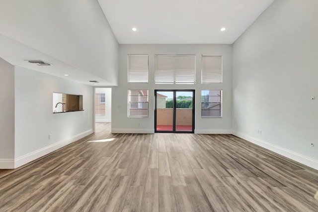 unfurnished living room with a towering ceiling and light hardwood / wood-style floors