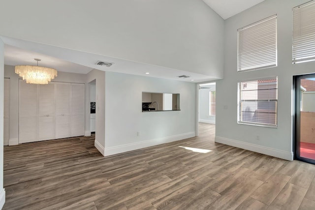 unfurnished living room featuring wood-type flooring, a high ceiling, and an inviting chandelier