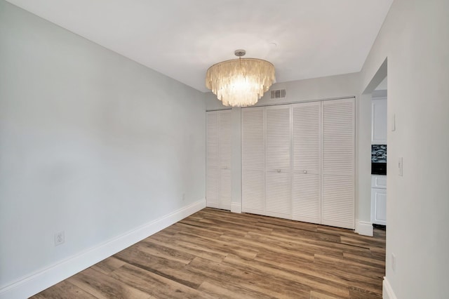 unfurnished bedroom featuring a closet, wood-type flooring, and a chandelier