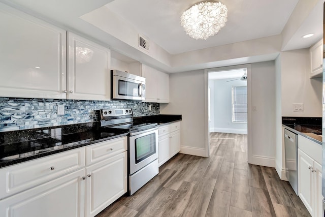 kitchen with white cabinets, stainless steel appliances, dark stone counters, and tasteful backsplash