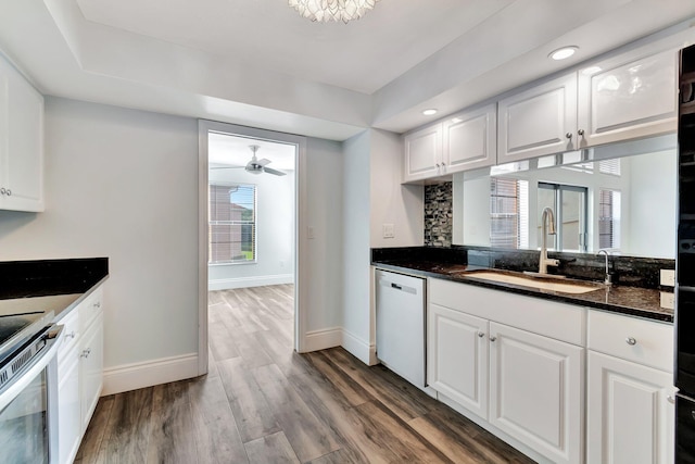 kitchen featuring white dishwasher, sink, wood-type flooring, dark stone countertops, and white cabinetry