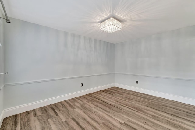 empty room featuring wood-type flooring and a notable chandelier