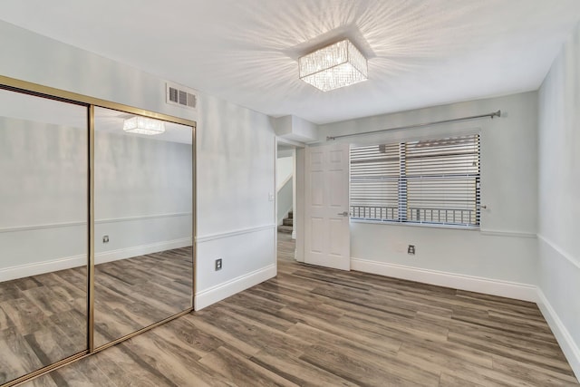 unfurnished bedroom with a closet, wood-type flooring, and a notable chandelier