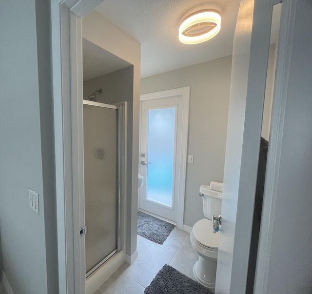 bathroom with tile patterned flooring, toilet, and a shower with shower door