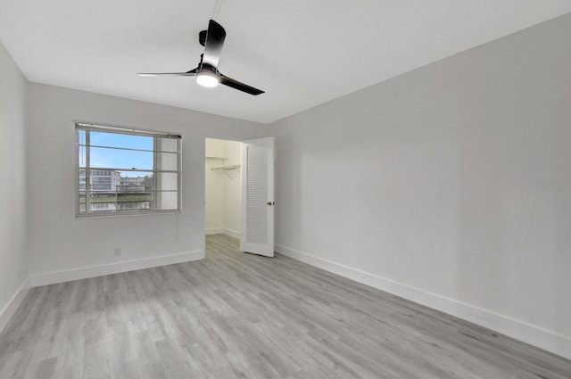 unfurnished bedroom with a walk in closet, ceiling fan, a closet, and light wood-type flooring