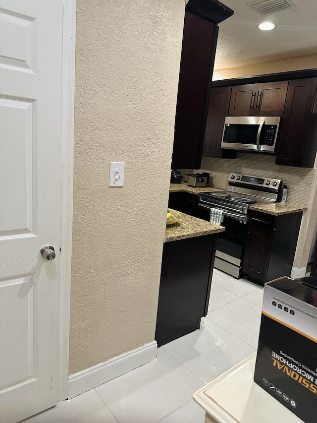 kitchen featuring light stone countertops, light tile patterned floors, dark brown cabinetry, and stainless steel appliances