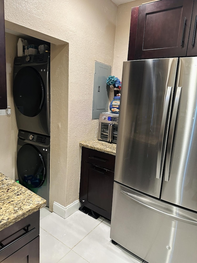 kitchen with light stone counters, stacked washer and dryer, electric panel, stainless steel refrigerator, and light tile patterned flooring