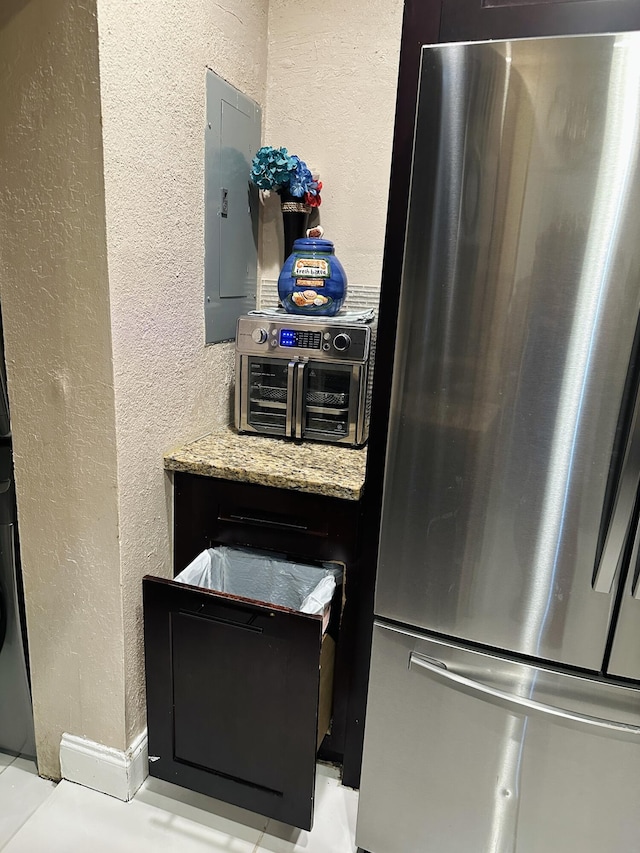 kitchen with stainless steel refrigerator, light stone counters, and electric panel