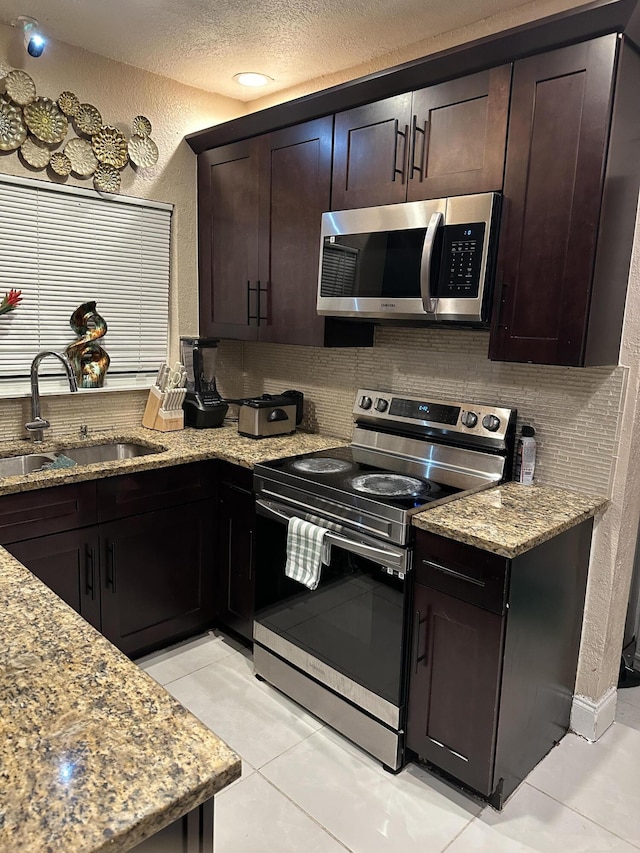 kitchen with light stone countertops, dark brown cabinetry, stainless steel appliances, sink, and light tile patterned flooring