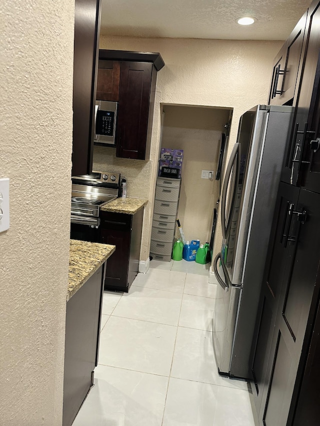 kitchen with light stone counters, dark brown cabinets, light tile patterned flooring, and appliances with stainless steel finishes