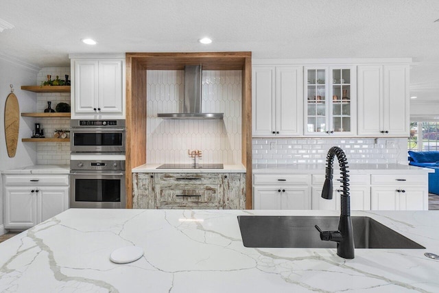 kitchen with backsplash, wall chimney exhaust hood, double oven, white cabinets, and light stone counters