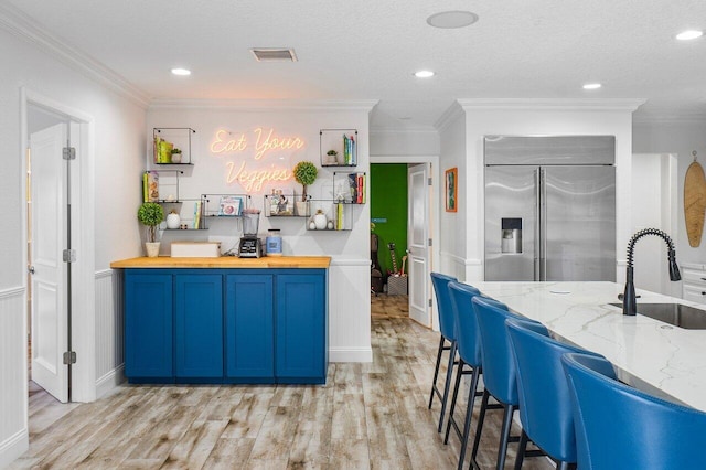 kitchen with crown molding, stainless steel built in refrigerator, light stone counters, and sink