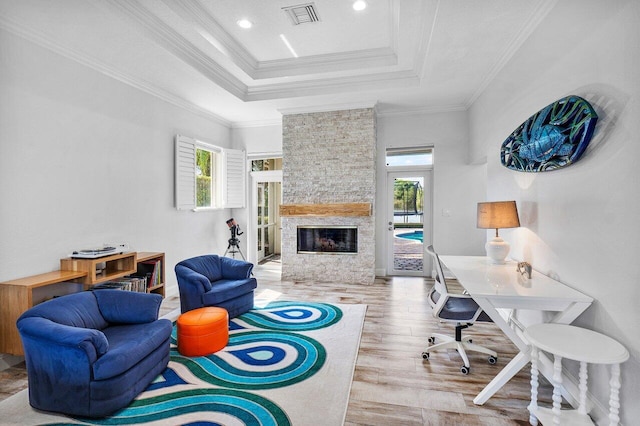 living room featuring a raised ceiling, a stone fireplace, ornamental molding, and hardwood / wood-style floors