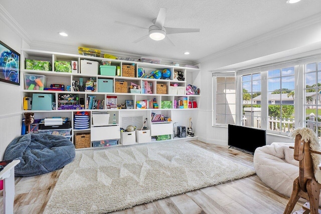 playroom featuring a textured ceiling, ceiling fan, ornamental molding, and light hardwood / wood-style flooring