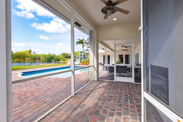 unfurnished sunroom featuring ceiling fan, a water view, and a swimming pool