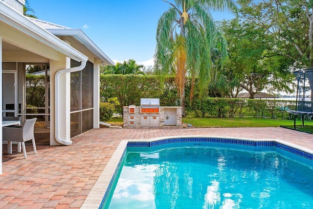 view of pool with a trampoline, a sunroom, exterior kitchen, grilling area, and a patio