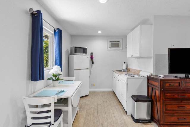 kitchen with an AC wall unit, white appliances, washer / dryer, white cabinetry, and light hardwood / wood-style flooring