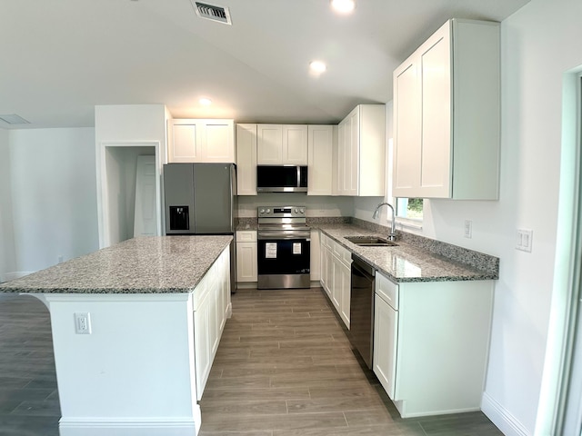 kitchen with appliances with stainless steel finishes, dark stone counters, sink, white cabinets, and a kitchen island