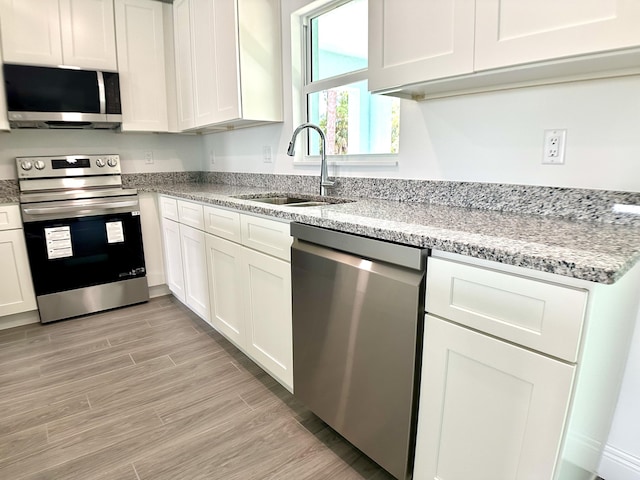 kitchen with light stone countertops, white cabinetry, sink, and stainless steel appliances