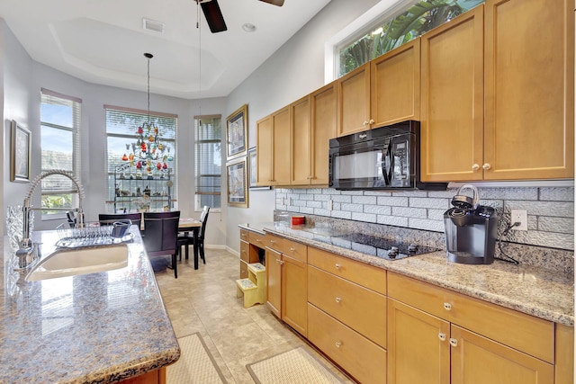 kitchen featuring sink, light stone counters, decorative light fixtures, a tray ceiling, and black appliances