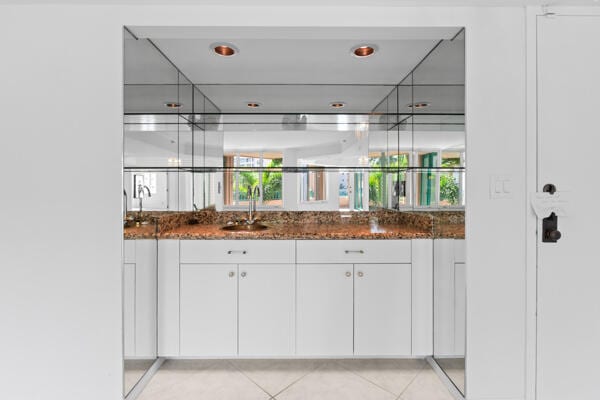 bar with white cabinetry, light tile patterned flooring, sink, and dark stone countertops