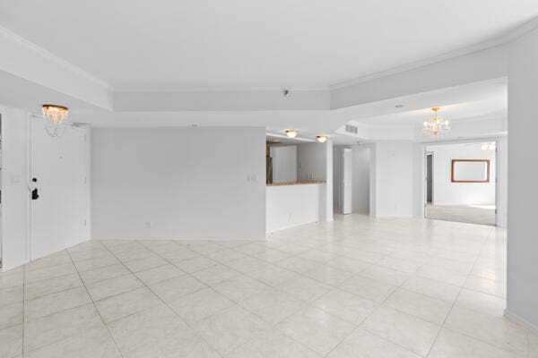 unfurnished room with a raised ceiling, ornamental molding, and an inviting chandelier