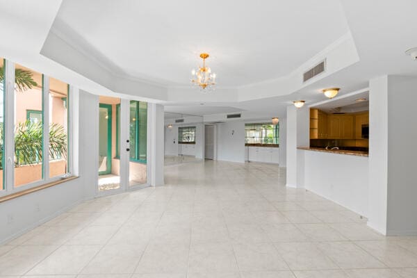 unfurnished living room featuring a raised ceiling, light tile patterned floors, and a notable chandelier