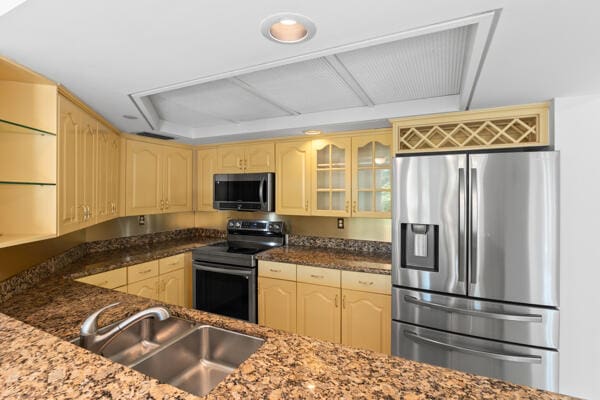 kitchen with stainless steel appliances, light brown cabinetry, sink, and dark stone counters