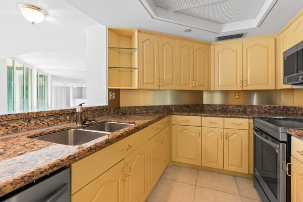 kitchen featuring sink, light tile patterned floors, stainless steel appliances, a tray ceiling, and light brown cabinetry