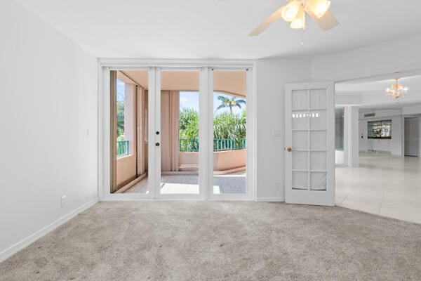 empty room featuring ceiling fan with notable chandelier and light carpet