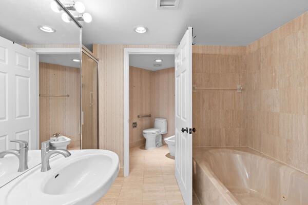 bathroom with tile patterned floors, toilet, sink, a bidet, and a tub
