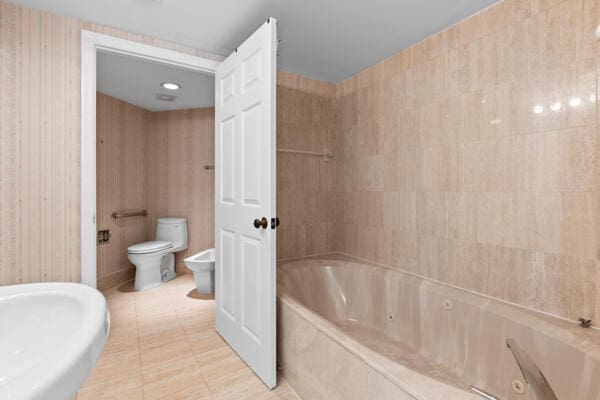 bathroom with a bidet, toilet, tile patterned flooring, and a bath