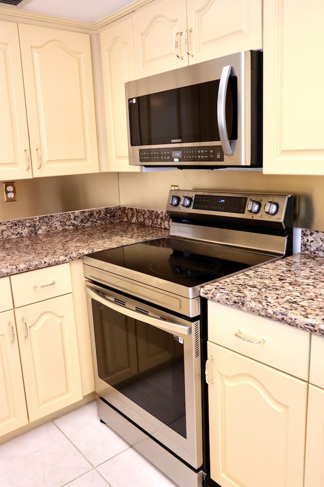 kitchen with light tile patterned floors, stainless steel appliances, dark stone counters, and cream cabinets