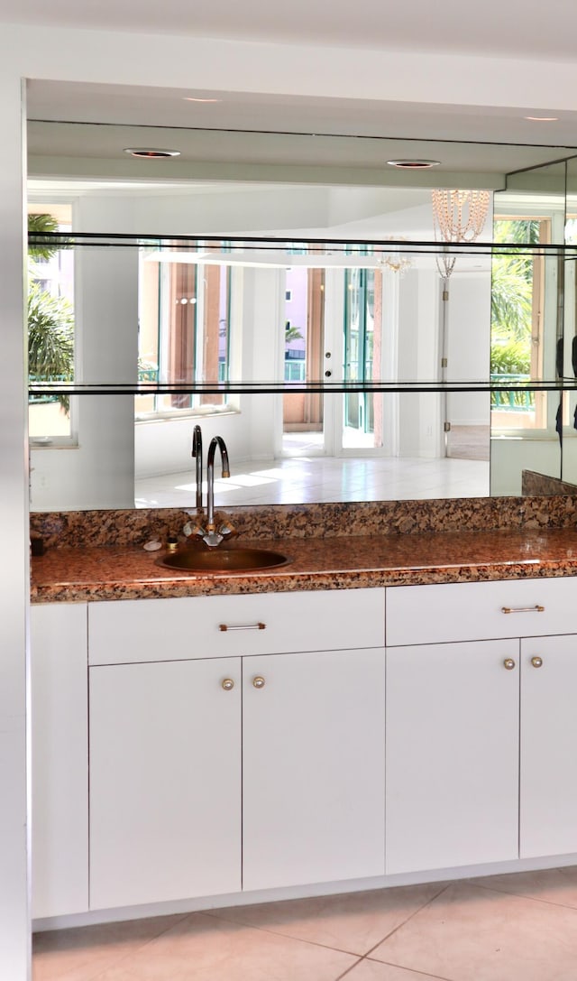 kitchen with white cabinets, light tile patterned floors, sink, and dark stone counters